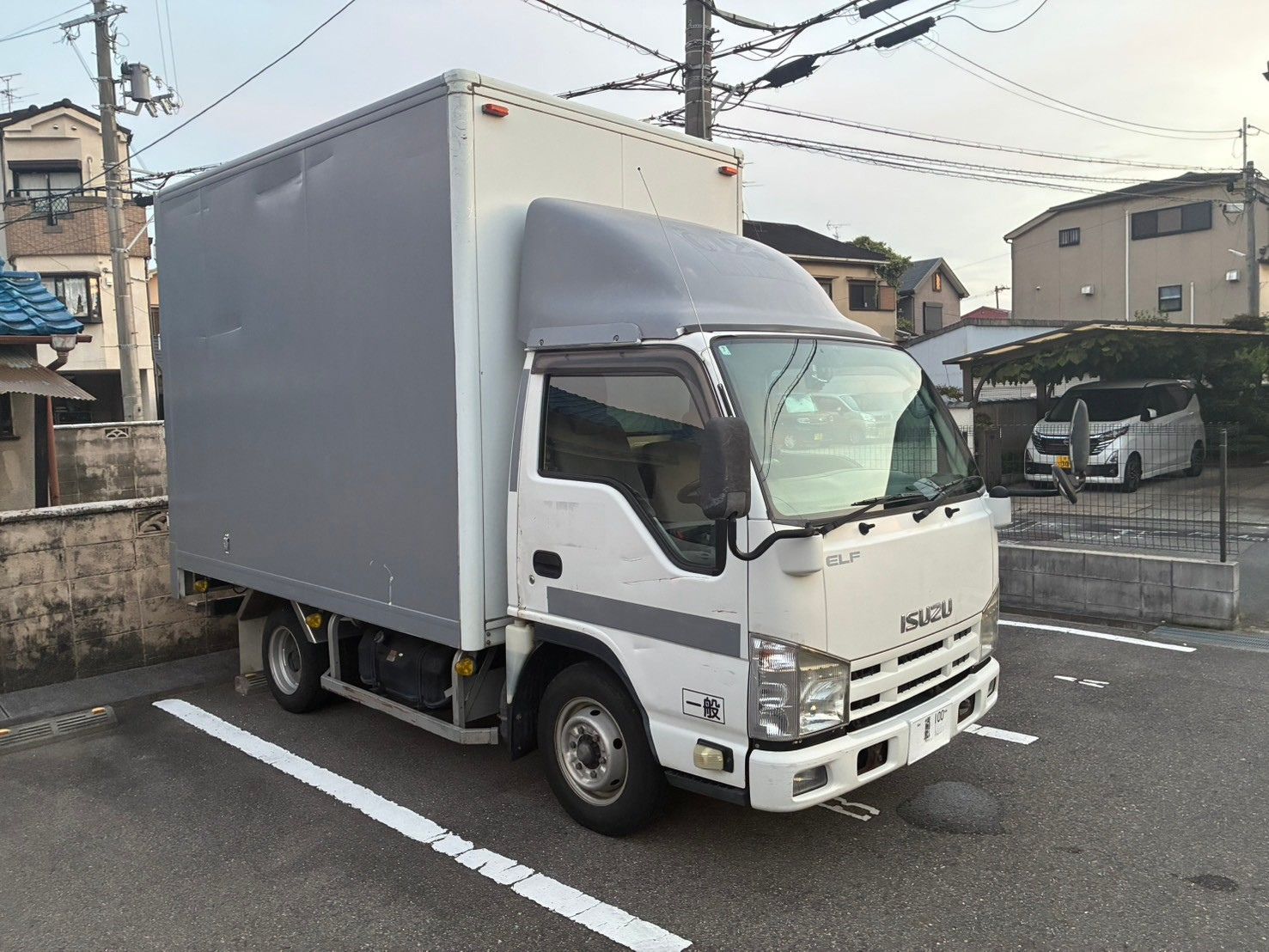 駐車場に停まる白いキャブとグレーの箱型荷台のトラックを右斜め前から撮影した全景
